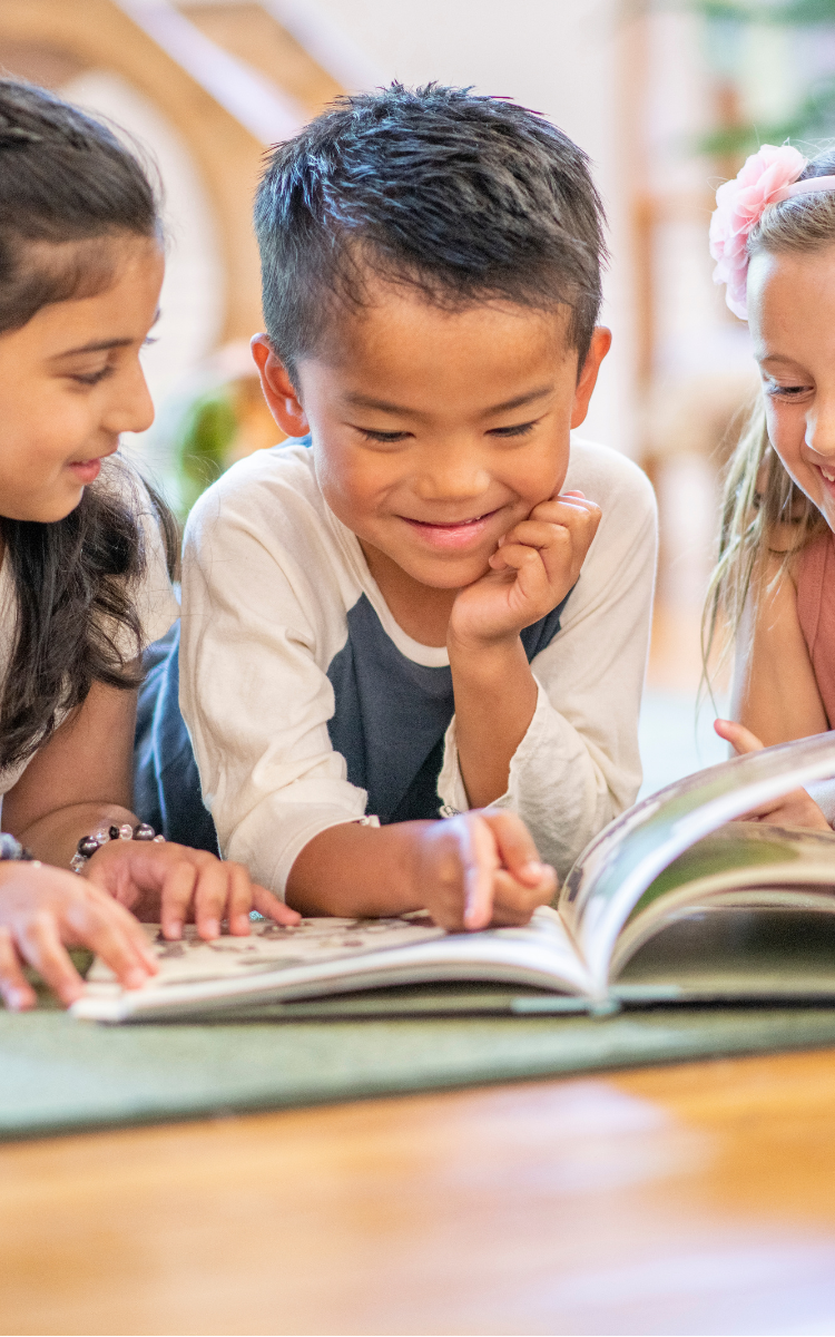 Group of three children laying on their bellies an reding a book together